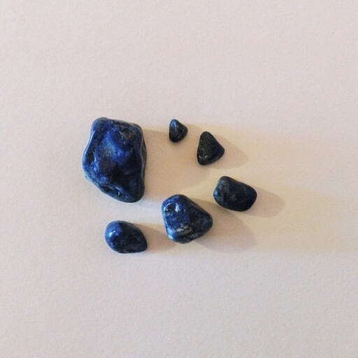 Shiny blue with gold and white flecks lapis lazuli rocks in different sizes on a white paper background 