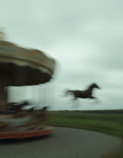 A heavily motion-blurred scene depicting a horse escaping a carousel ride in motion at high speed. The background features a cloudy, overcast sky and a grassy field extending to the horizon. The carousel is set on a circular, grey asphalt patch in the foreground.