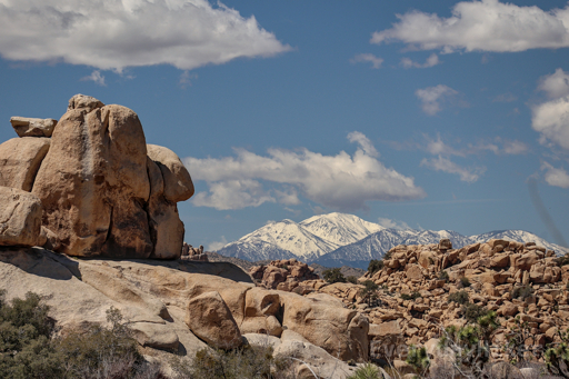 A few large boulders rise on the left of frame like a beacon with a large pile of boulders on the right. In between them a snow capped mountain may be seen in the distance.