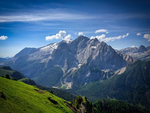 Marmolada con cime innevate e foresta verde sotto un cielo blu con nuvole bianche.