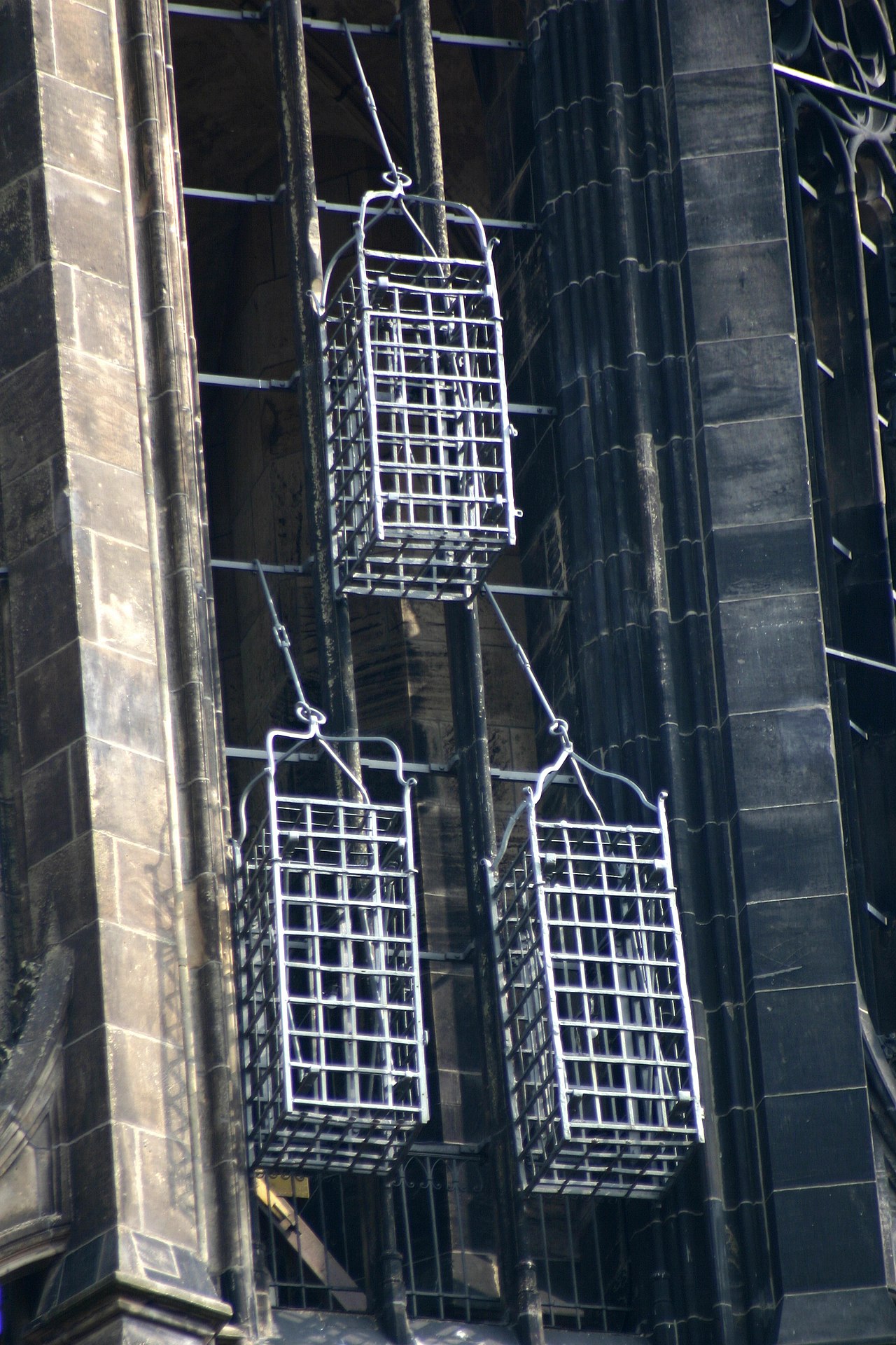 Three heavy metal cages suspended on the side of a church