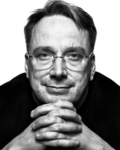 Ritratto in bianco e nero di Linus Torvalds. Ha capelli corti scuri con striature chiare. Indossa occhiali da vista con montatura metallica sottile. Le mani sono intrecciate sotto il mento, con un anello visibile su un dito. Lo sfondo è bianco e la persona indossa una maglia scura.