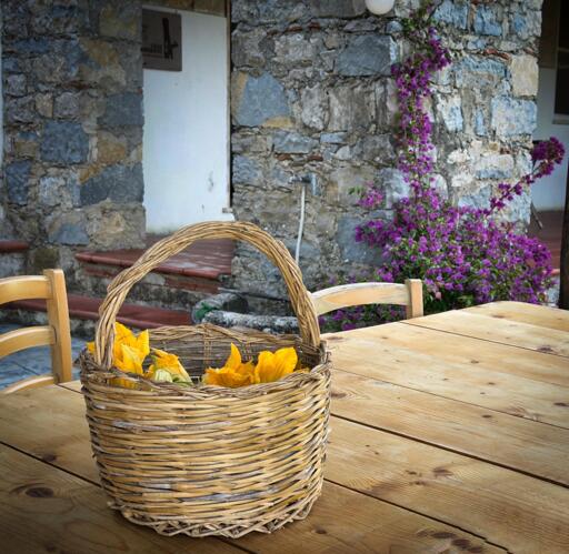 Cestino di vimini con fiori di zucca sul tavolo di legno, su uno sfondo di muri in pietra e fiori viola in giardino.
