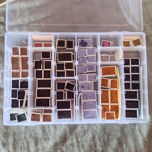 A plastic, segmented container with different sections holding watercolour paints in various colours.