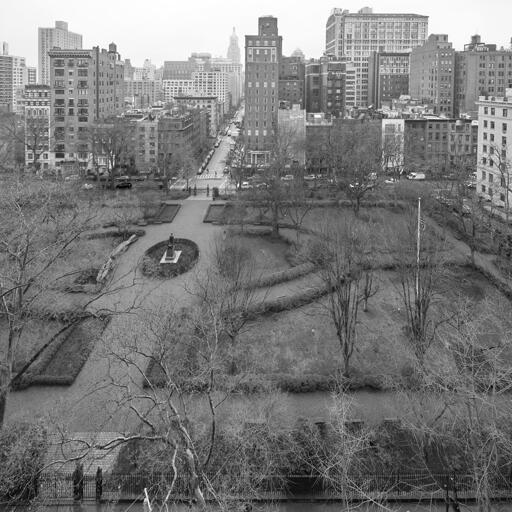 A fenced-in, formally landscaped urban park surrounded by buildings on a grey day. There are no people. You should leave now.