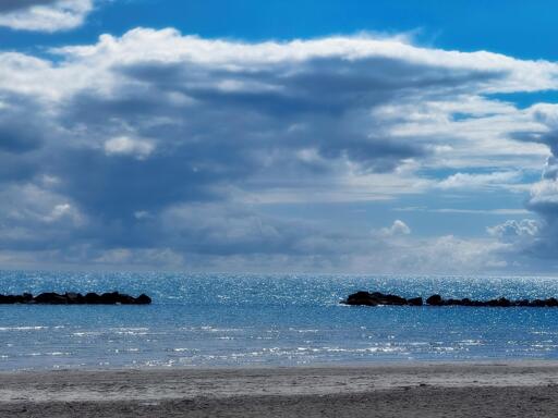 Spiaggia con scogli e mare calmo sotto un cielo nuvoloso.