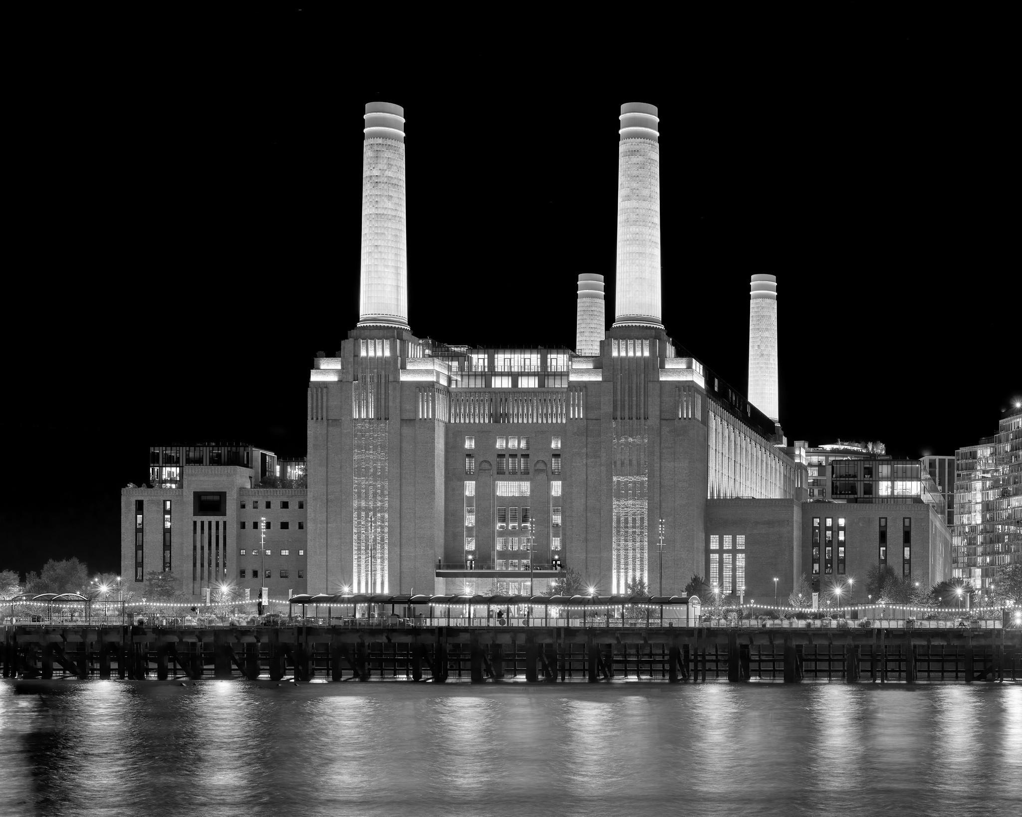 A large industrial building with four prominent smokestacks on each corner, across a river at night.