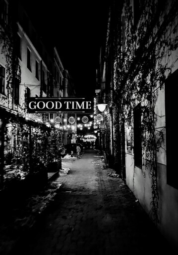 backyard of townhouses, in the dark, snow. obvious repurposing happening as restaurant can be seen to left, hanging lights ahead, ivy-covered wall to right. a huge sign saying "good time" is hanging over the yard